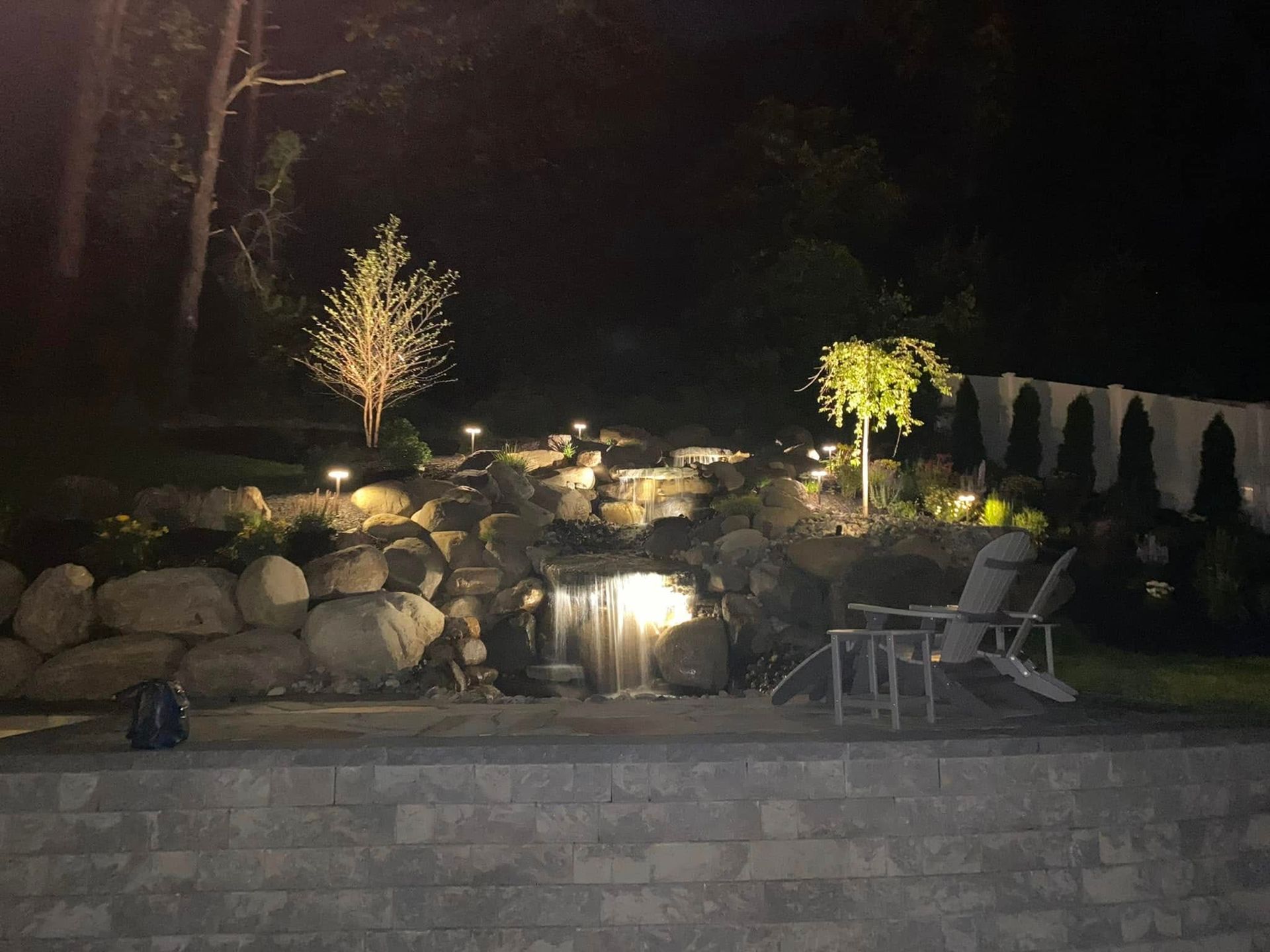 A patio area with chairs and a waterfall at night.