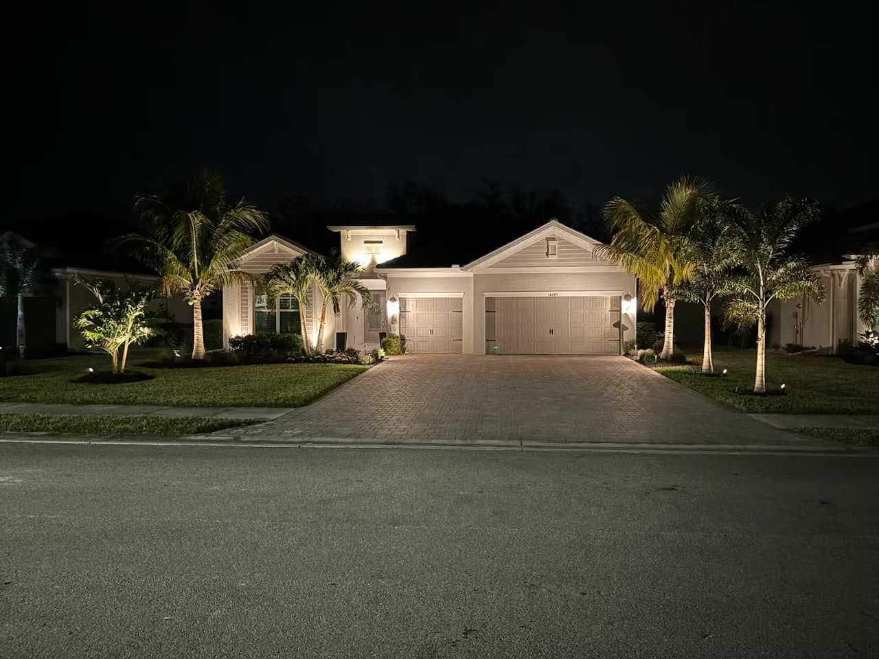 A house is lit up at night with palm trees in front of it