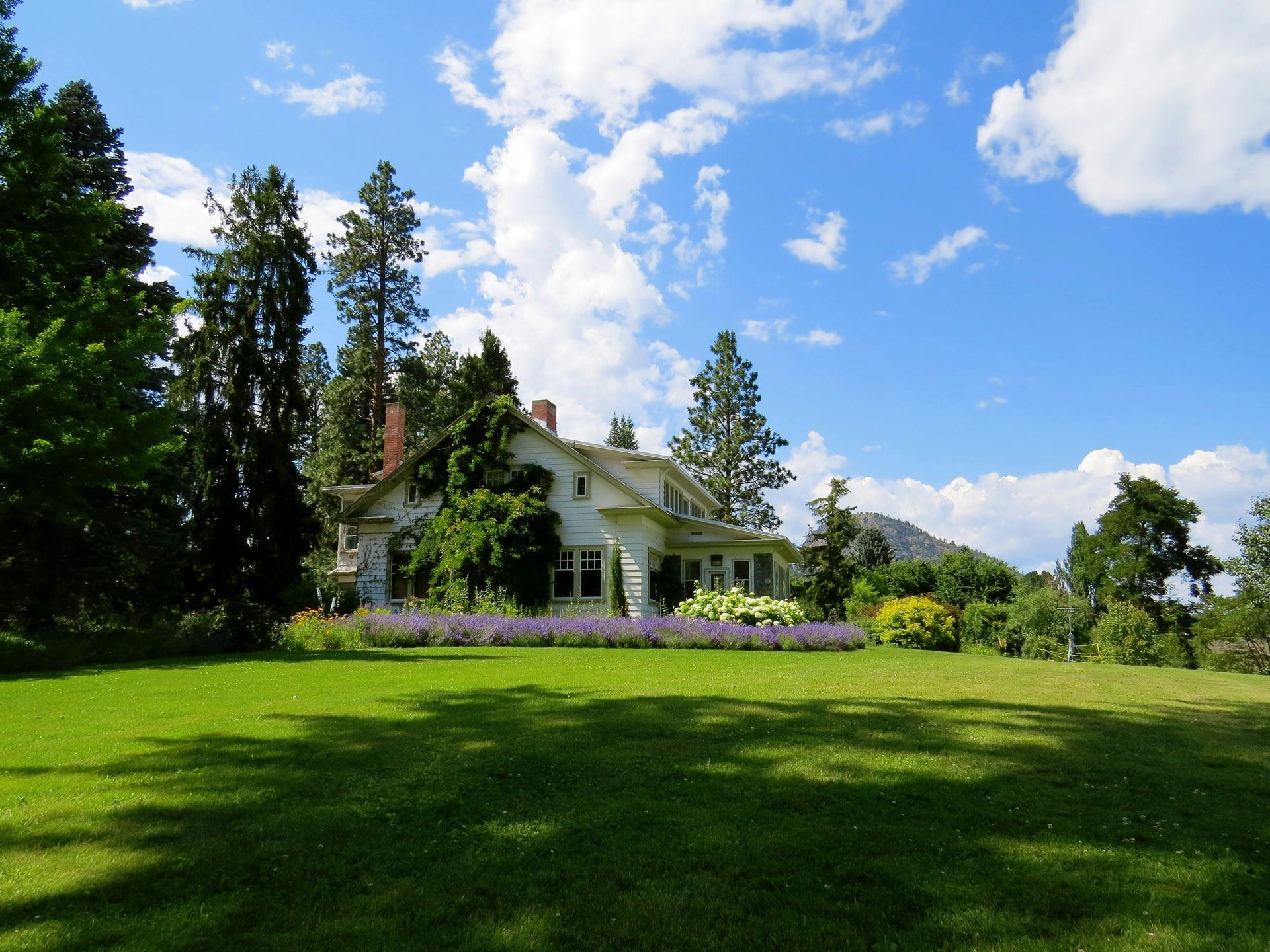 White house with a green lawn and trees under a blue sky with clouds.