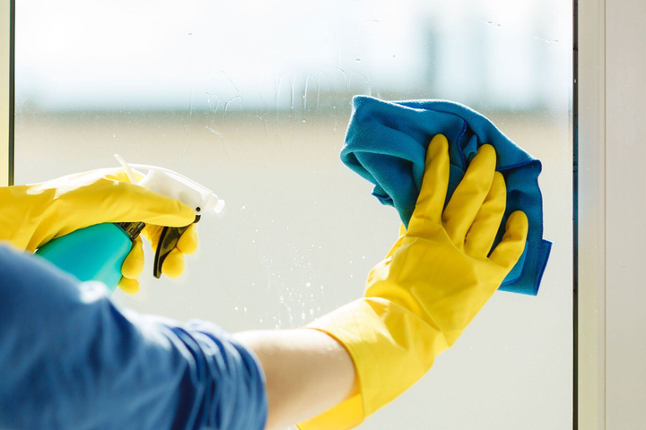 A person wearing yellow gloves is cleaning a window with a cloth.