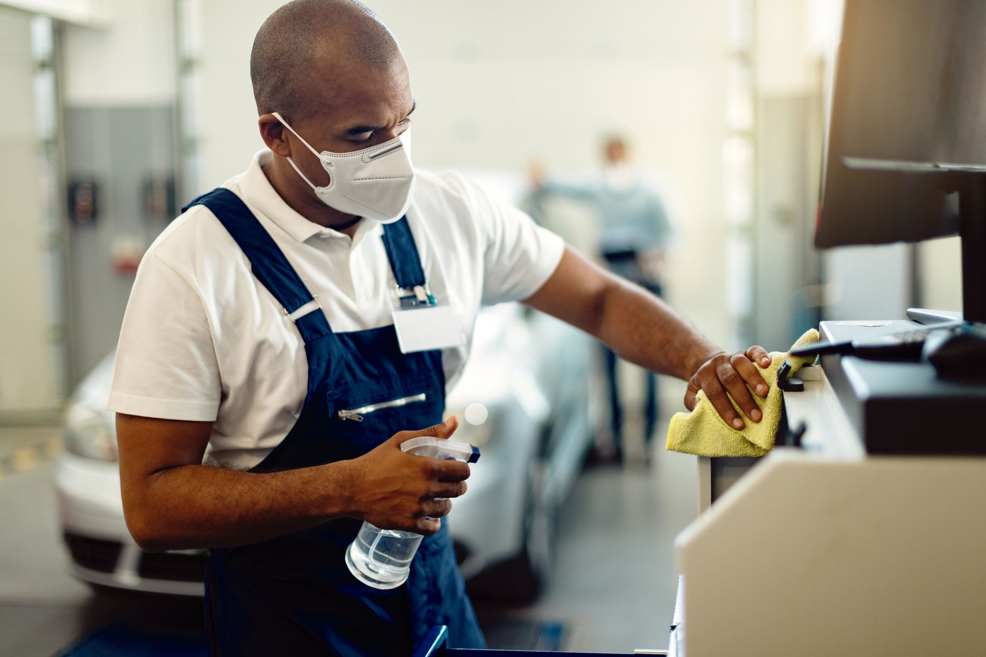 A man wearing a mask is cleaning a machine in a garage.