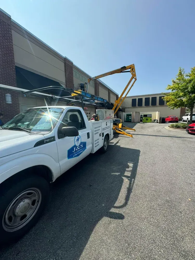 White work truck with a yellow boom lift reaching toward a building.