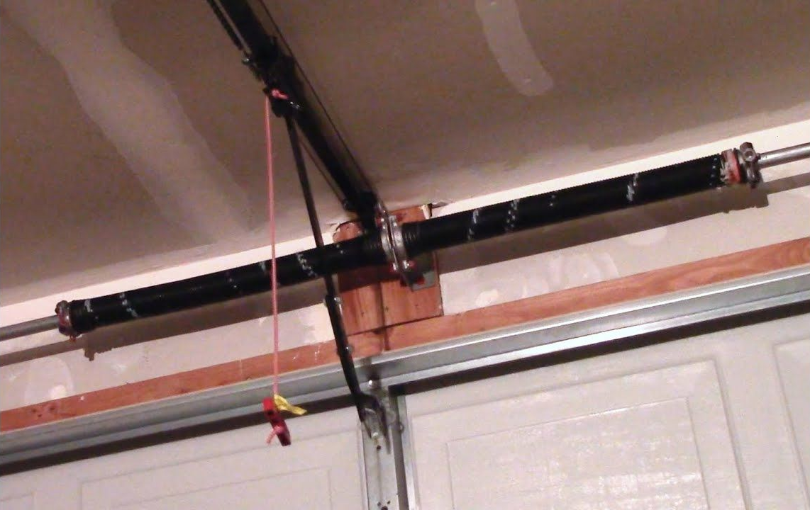 Garage door torsion spring system with black spring, pulleys, and a safety cable.