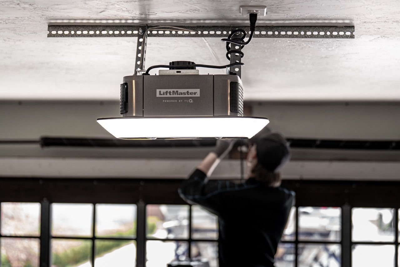 Two workers in safety gear installing a white garage door in a well-lit, industrial setting.