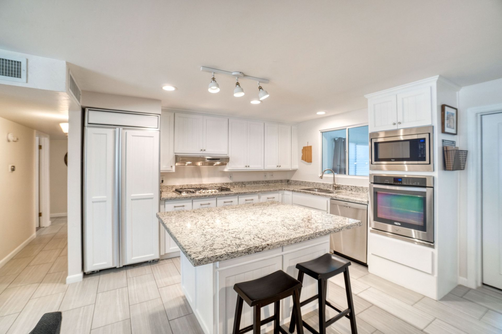 A kitchen with white cabinets , granite counter tops , stainless steel appliances and a large island.