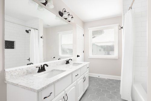 A bathroom with two sinks , a shower , and a window.