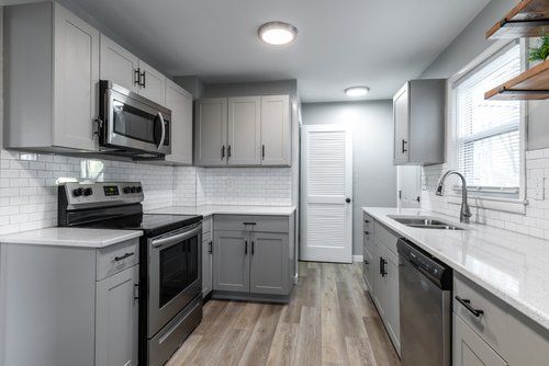 A kitchen with gray cabinets , stainless steel appliances , a sink , and a window.