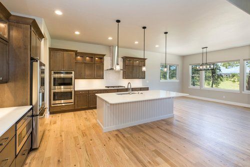 An empty kitchen with hardwood floors and stainless steel appliances.