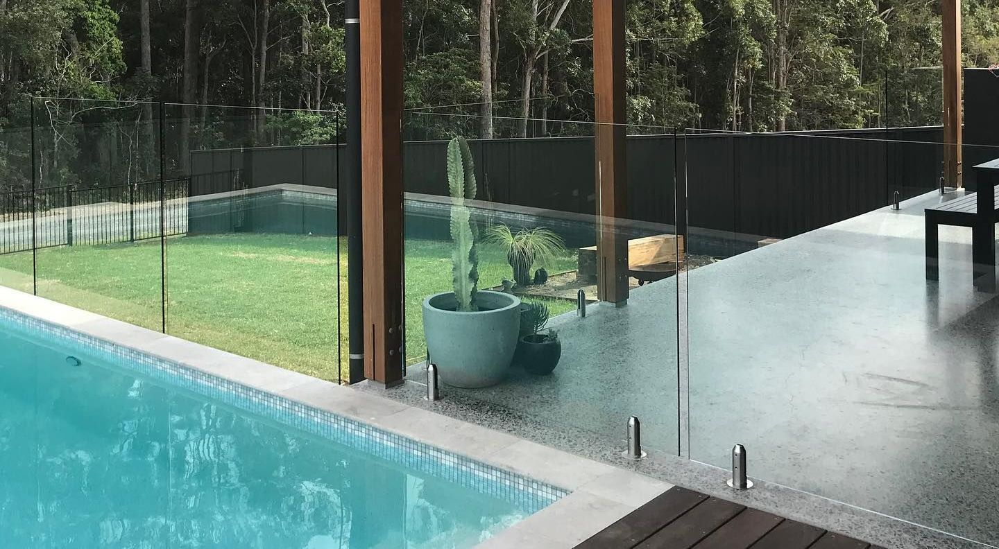 A Swimming Pool With a Glass Fence Around It and a Wooden Deck — Swift Glass & Aluminium In Woolgoolga, NSW