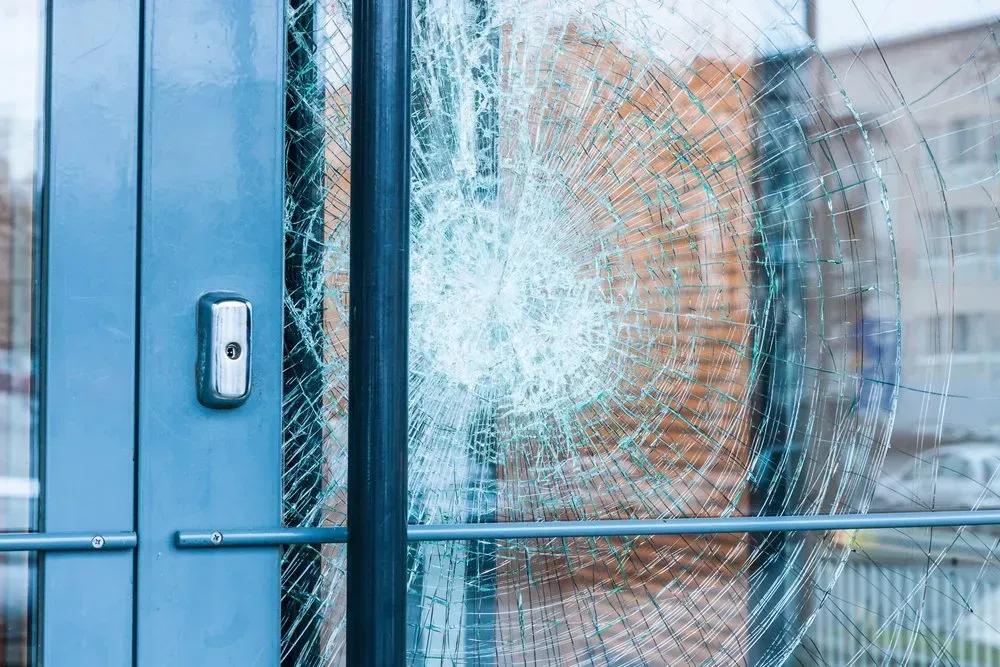 A Close Up of a Broken Glass Door With a Brick Building — Swift Glass & Aluminium In Woolgoolga, NSW