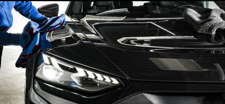 A man is cleaning a black car with a cloth.