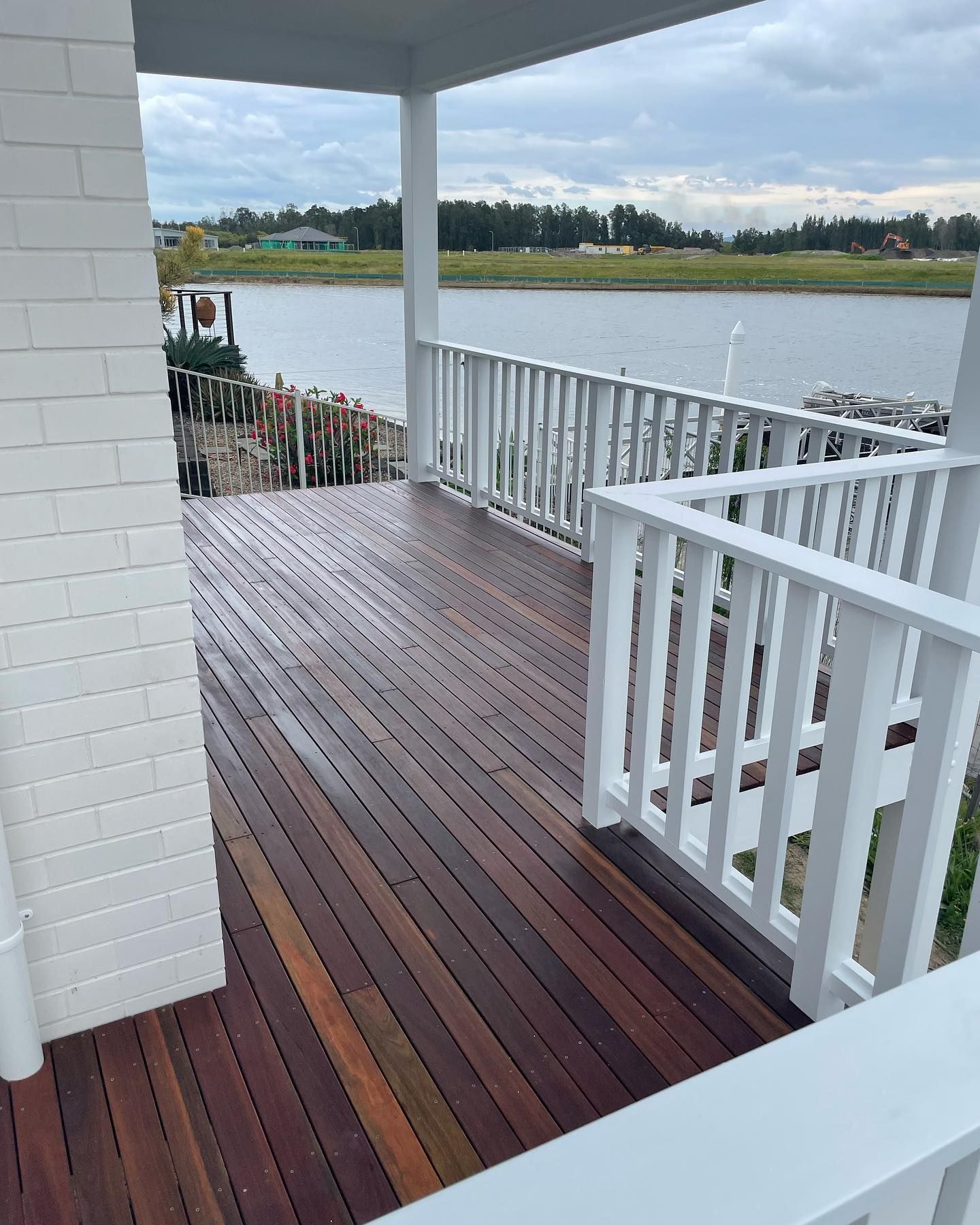 A Wooden Deck With White Railings, Brick Wall, and View of a Lake — All Coast Painting in Tweed Heads South, NSW