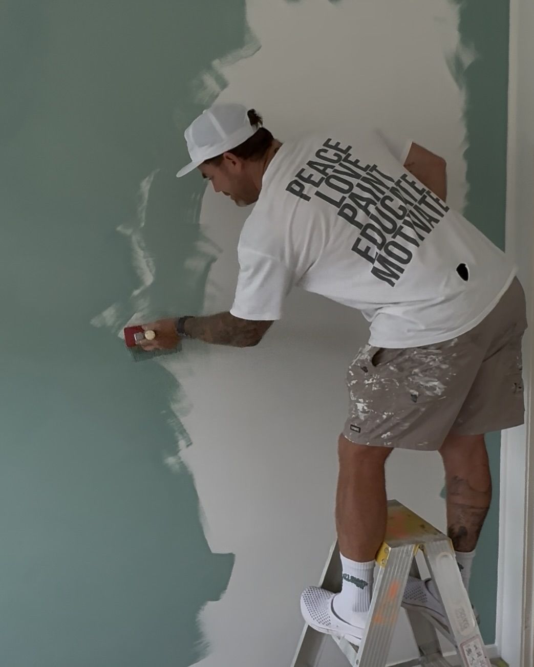 A Person on a Ladder, Painting a Microcement Wall with Sage Green Paint — All Coast Painting in Tweed Heads South, NSW