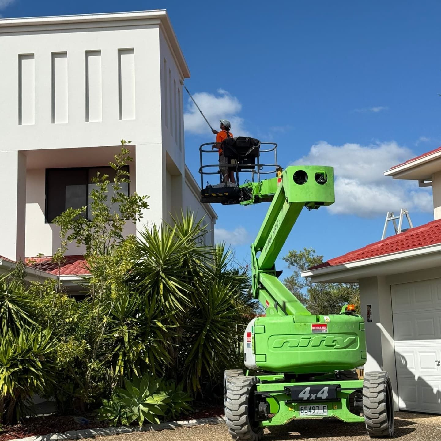 Person in Green Aerial Lift Working on White Building Under Blue Sky — All Coast Painting in Tweed Heads South, NSW