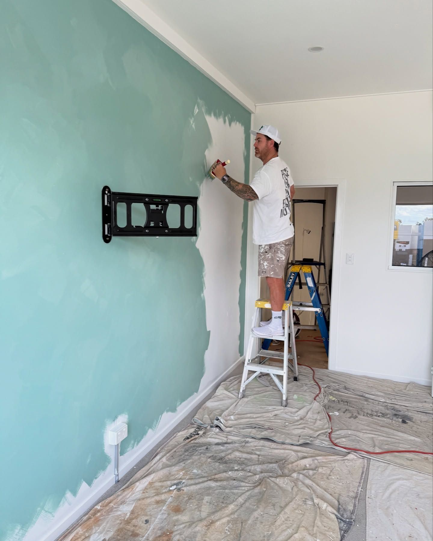 A Painter on a Ladder Applying Sage Green Finish to a Microcement Wall— All Coast Painting in Tweed Heads South, NSW
