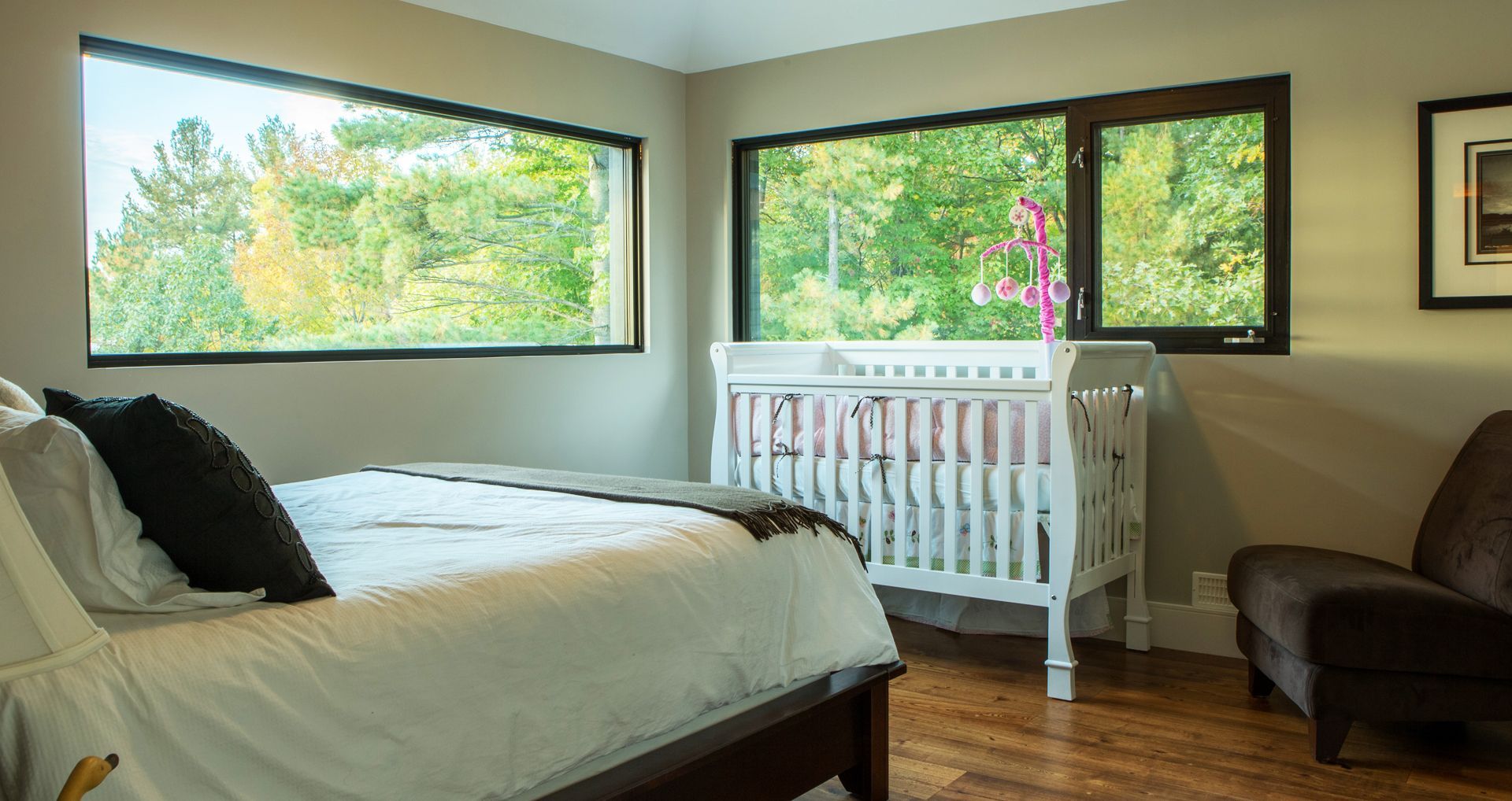 Family friendly custom cottage bedroom with bed, nursing chair and a baby's crib.