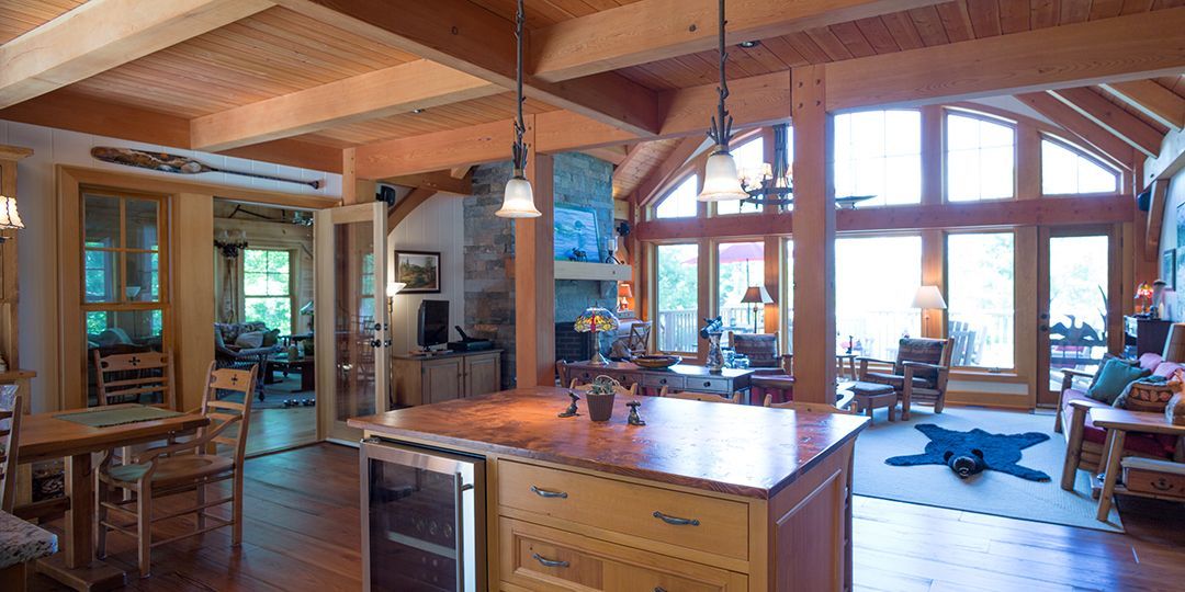 Open concept cottage showing kitchen, large windows and a stone fireplace.