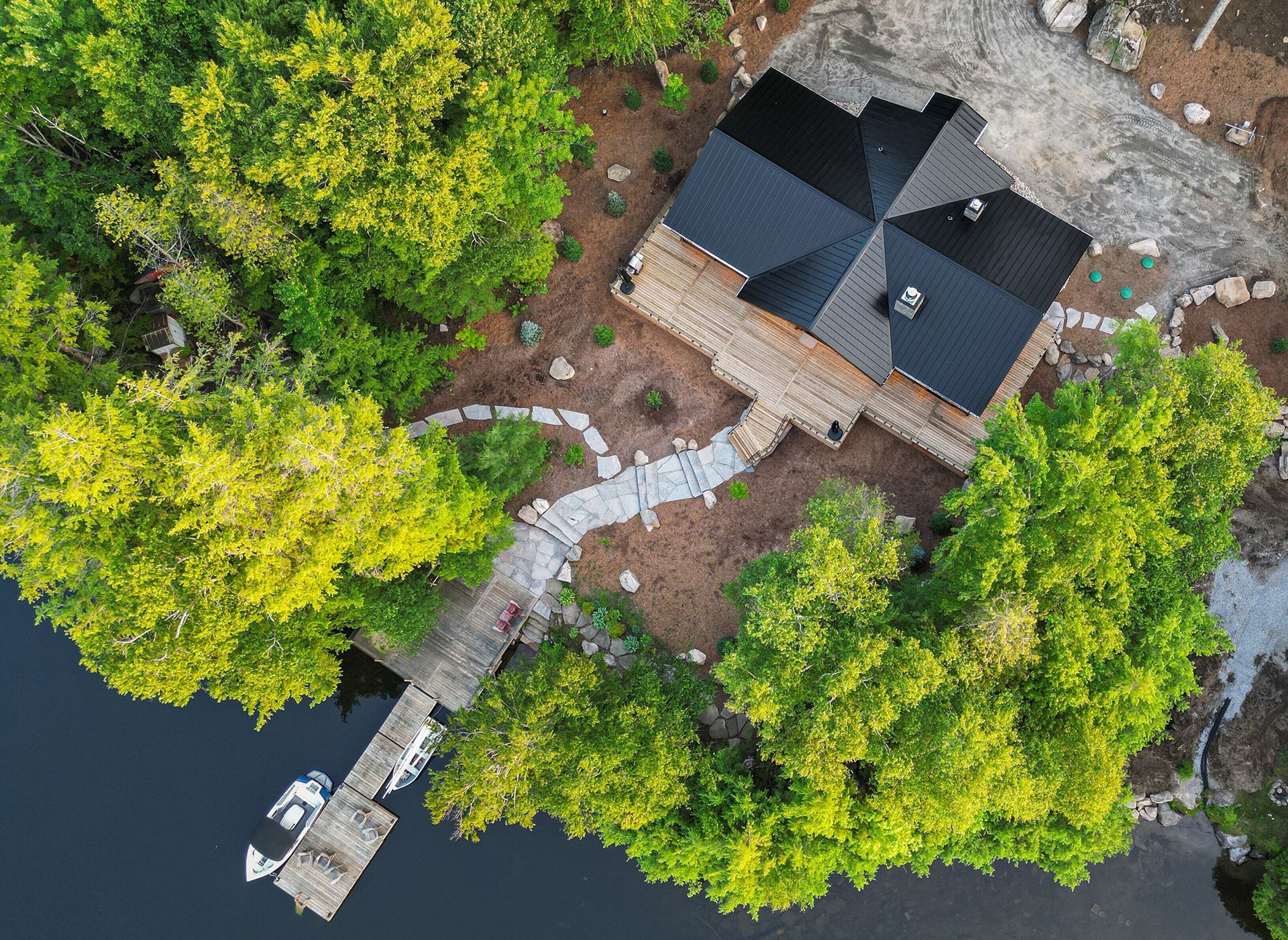 High view over a lakefront cottage, showing steel roofing, walkways, pier and lake.