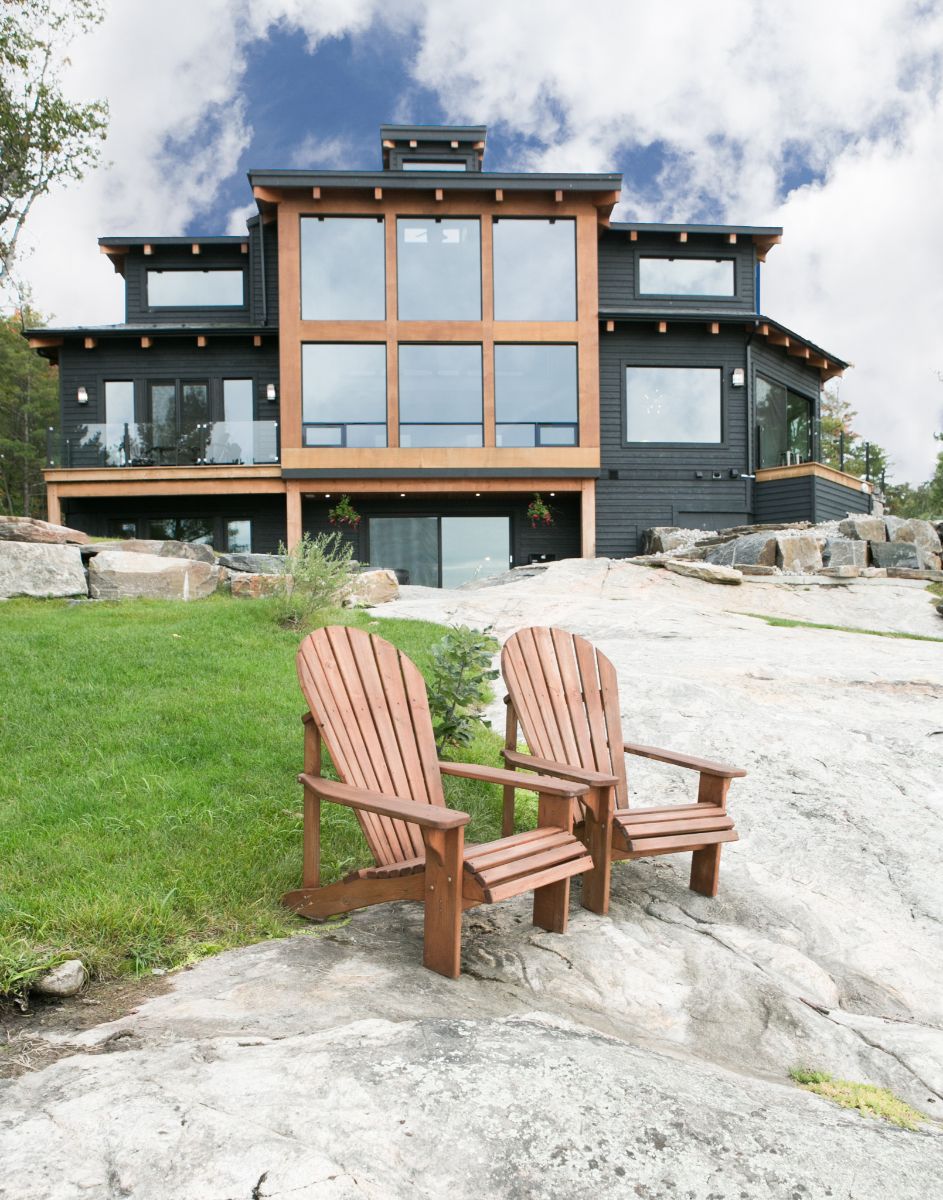 Two wooden chairs in front of a large Muskoka Cottage