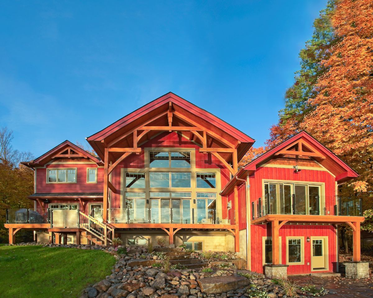 Custom Muskoka Cottage featuring a  large red house with a lot of windows is sitting on top of a hill.