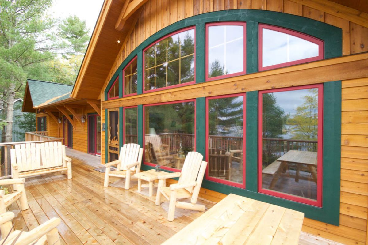 Custom Muskoka Cottage featuring a  large wooden house with lots of windows and chairs on the deck
