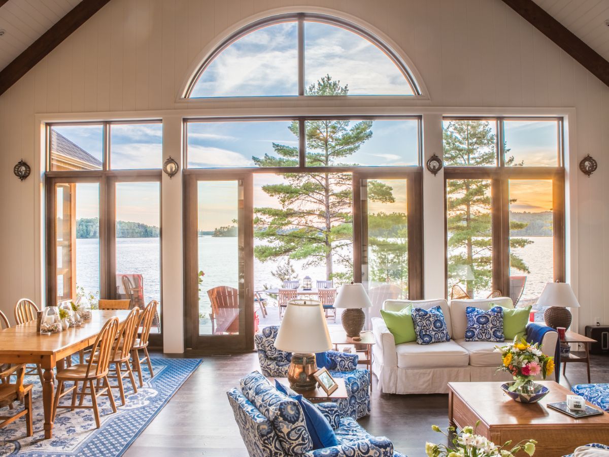Custom Muskoka Cottage featuring a  living room with a couch , chairs and a table with a view of a lake.
