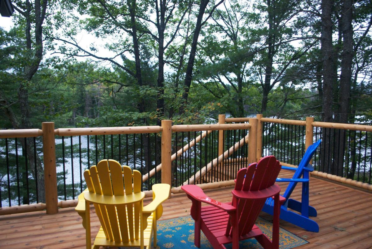 Three adirondack chairs are on a deck overlooking Lake Muskoka