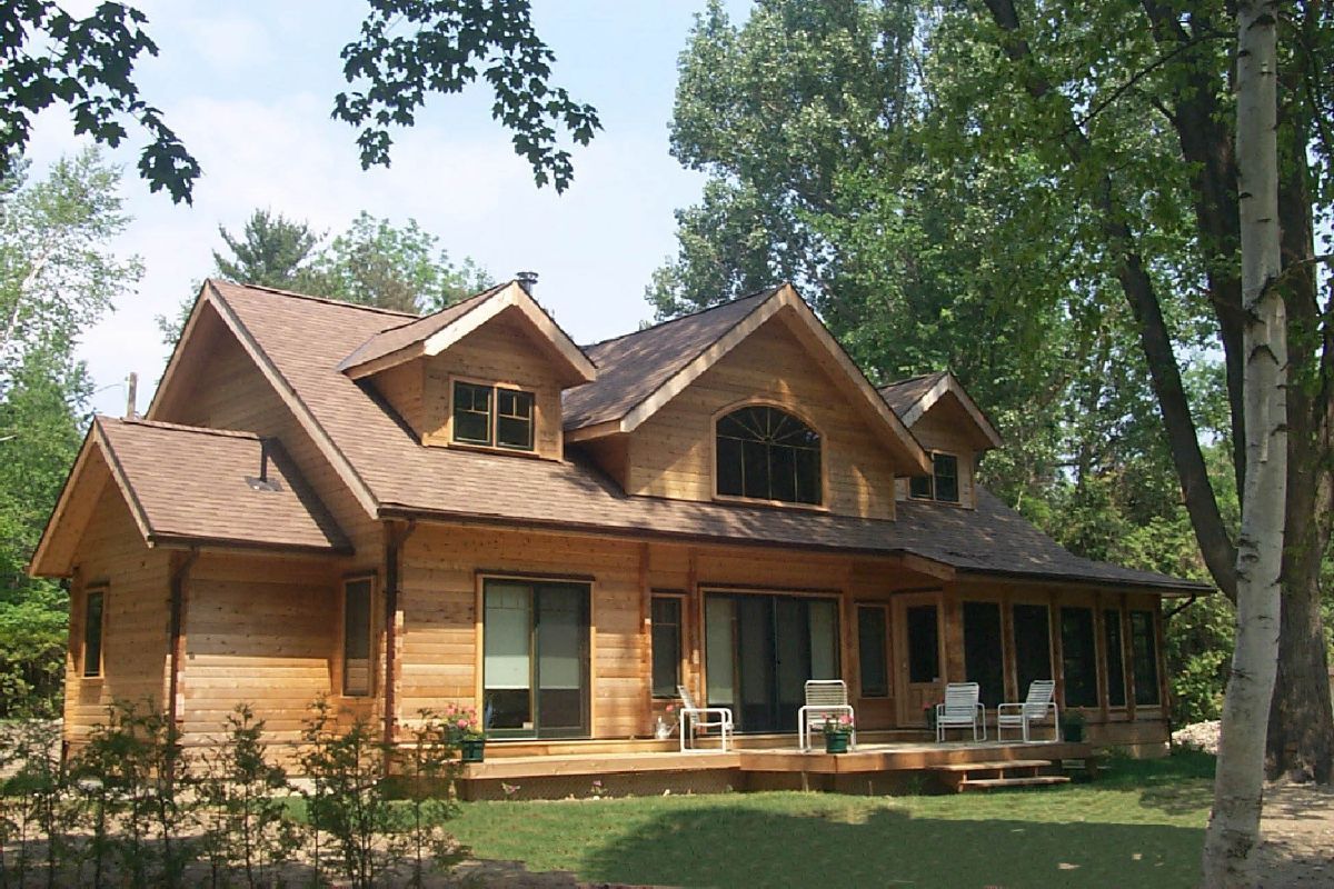 Custom Muskoka Cottage featuring a  large wooden house with a brown roof is surrounded by trees