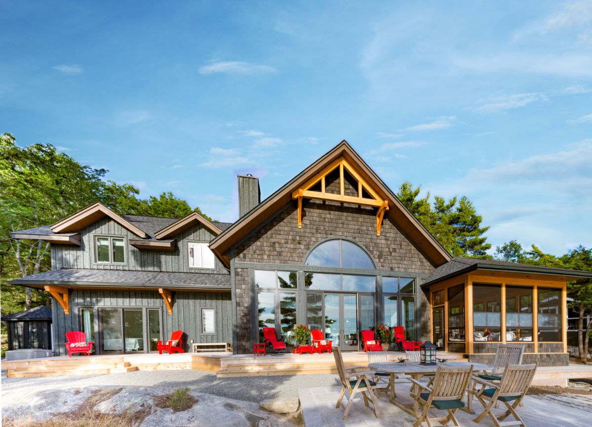 Custom Muskoka Cottage featuring a large house with a patio and chairs in front of it.