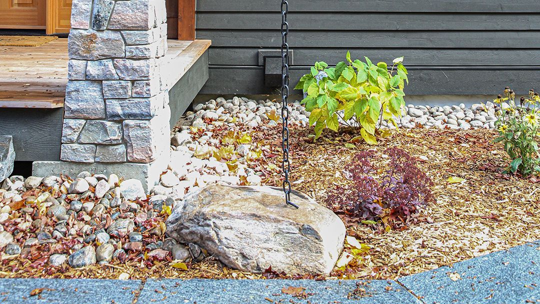 Front of a cottage porch showing a chain secured in a large rock to help water flow away from the foundation.