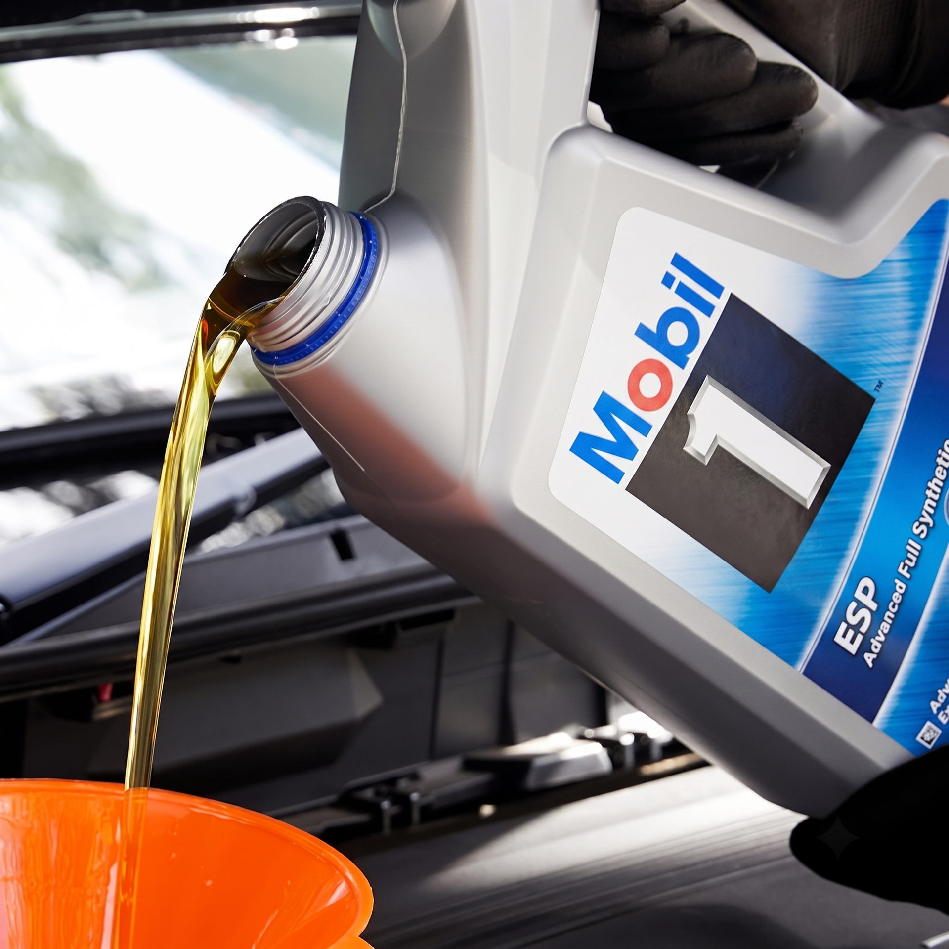Motor oil pouring from a Mobil 1 bottle into an orange funnel in a car engine bay