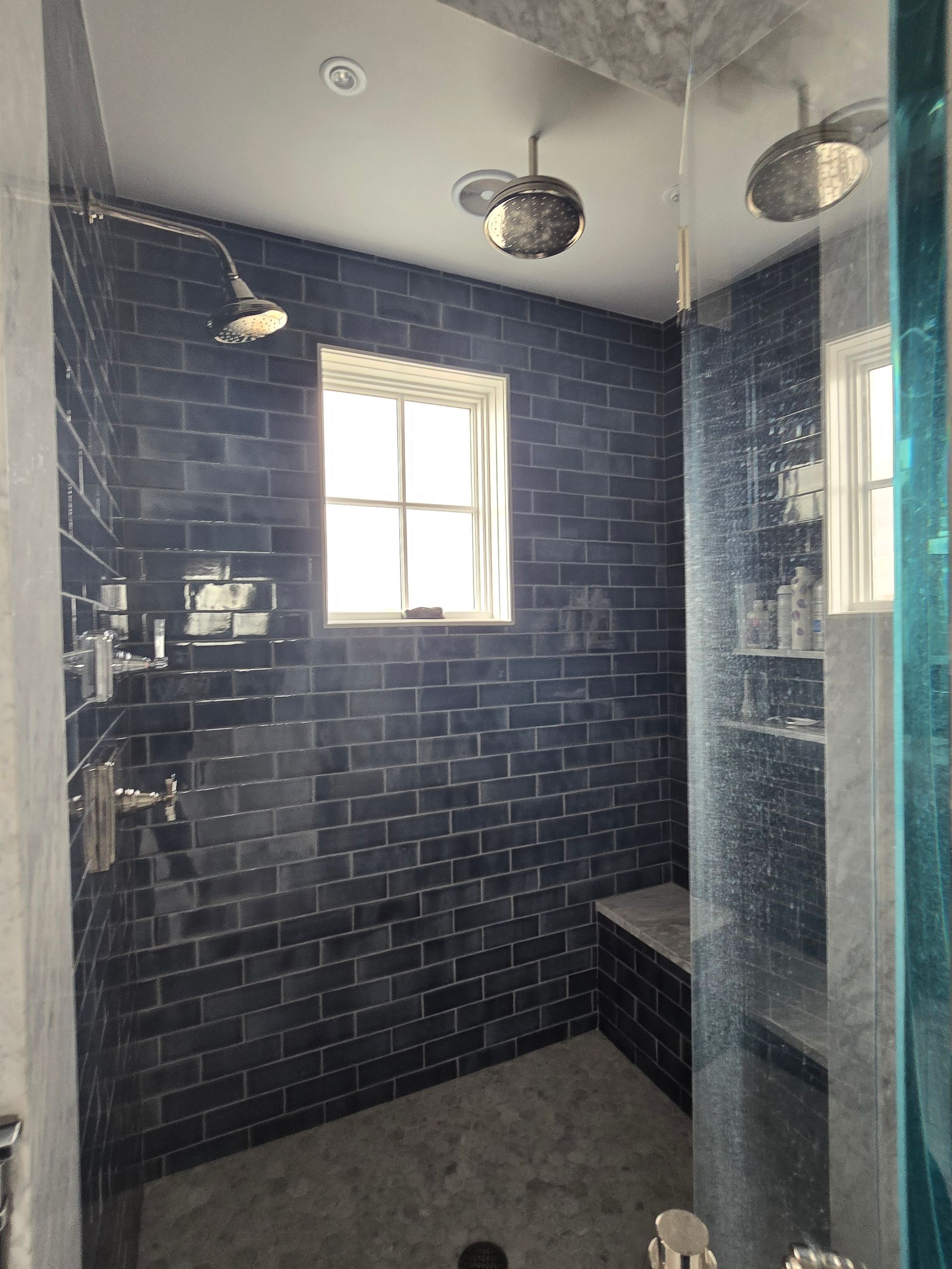 A walk in shower with blue tiles and a window