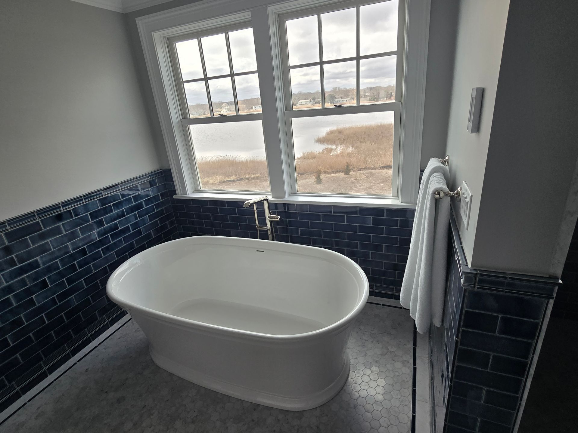 A bathtub in a bathroom with blue tiles and a window.