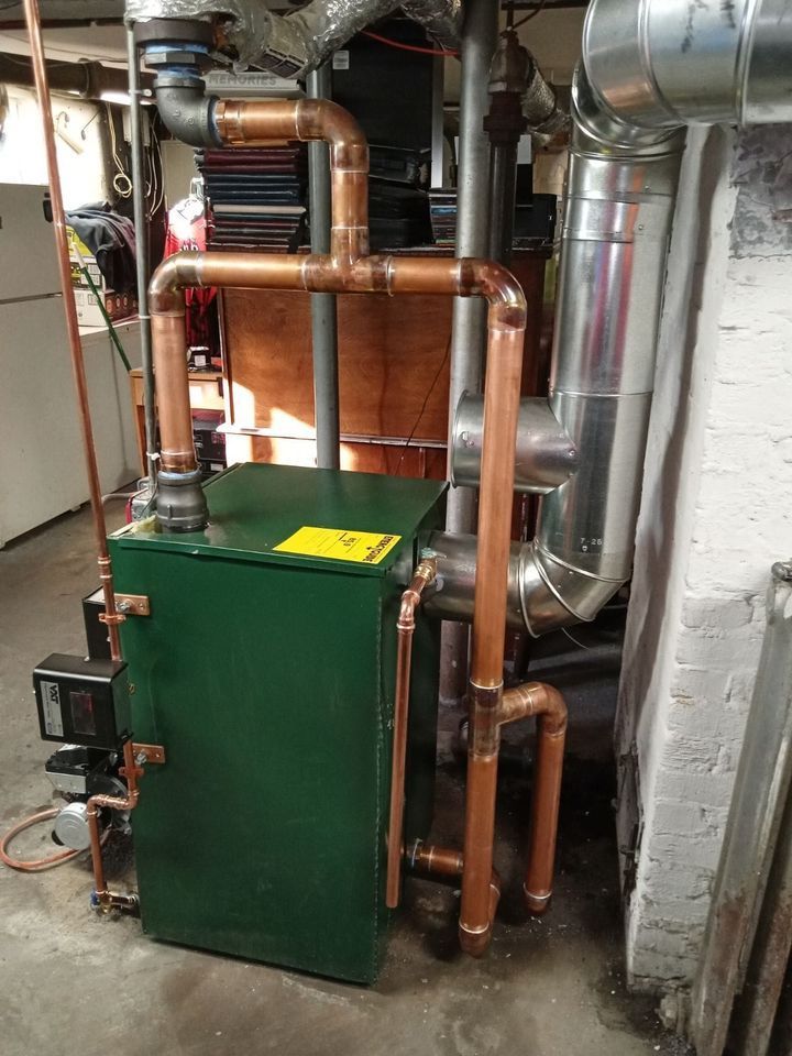 A green boiler with copper pipes attached to it is in a basement.
