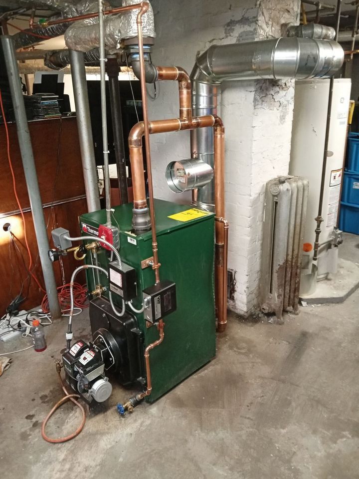 A green boiler with copper pipes attached to it is sitting in a basement.