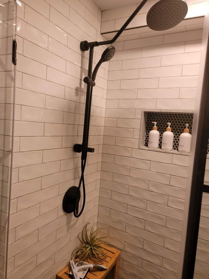 A shower with white tiles and a black shower head.