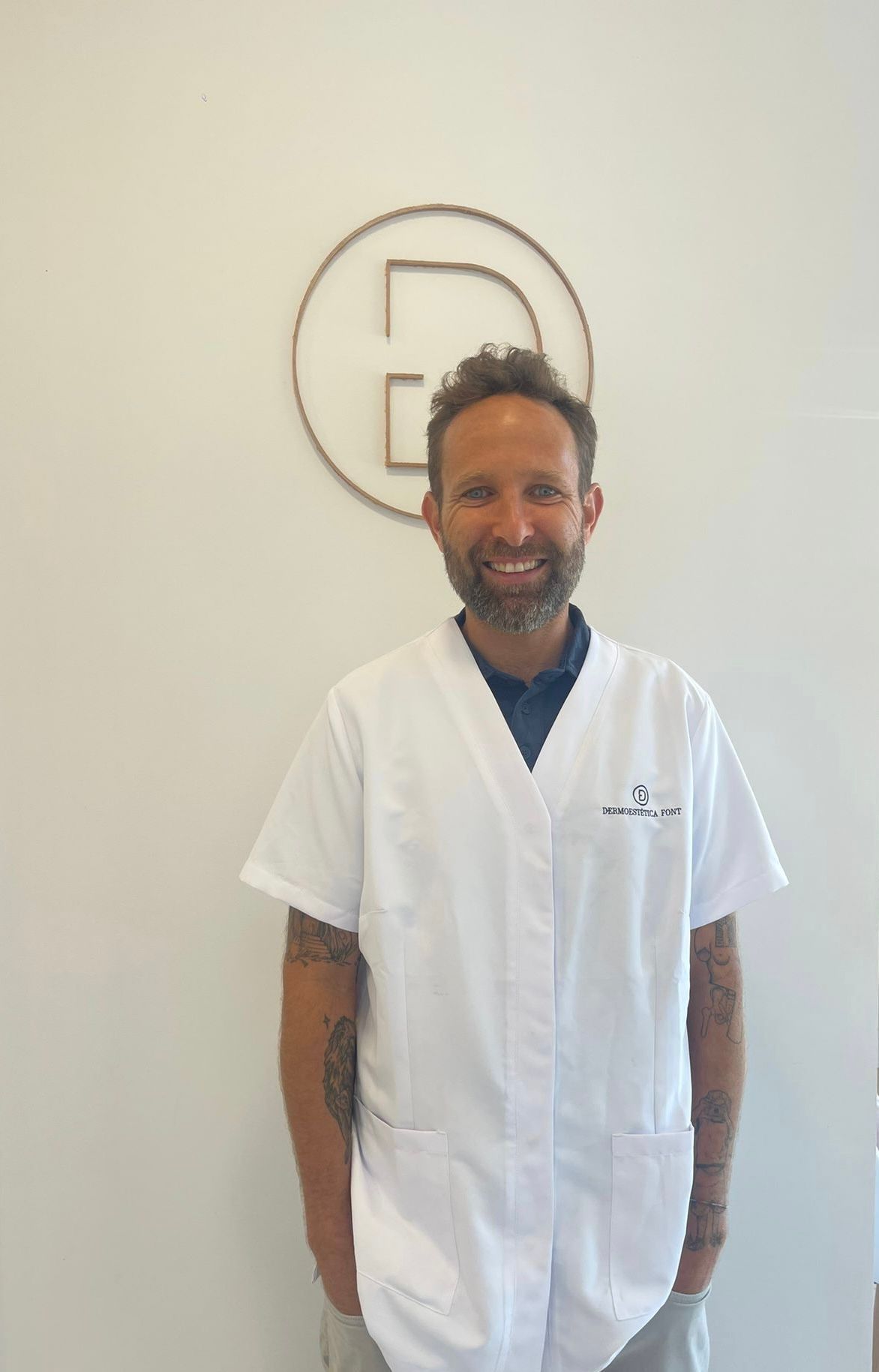 Un hombre con una bata de laboratorio blanca está parado frente a una pared blanca.