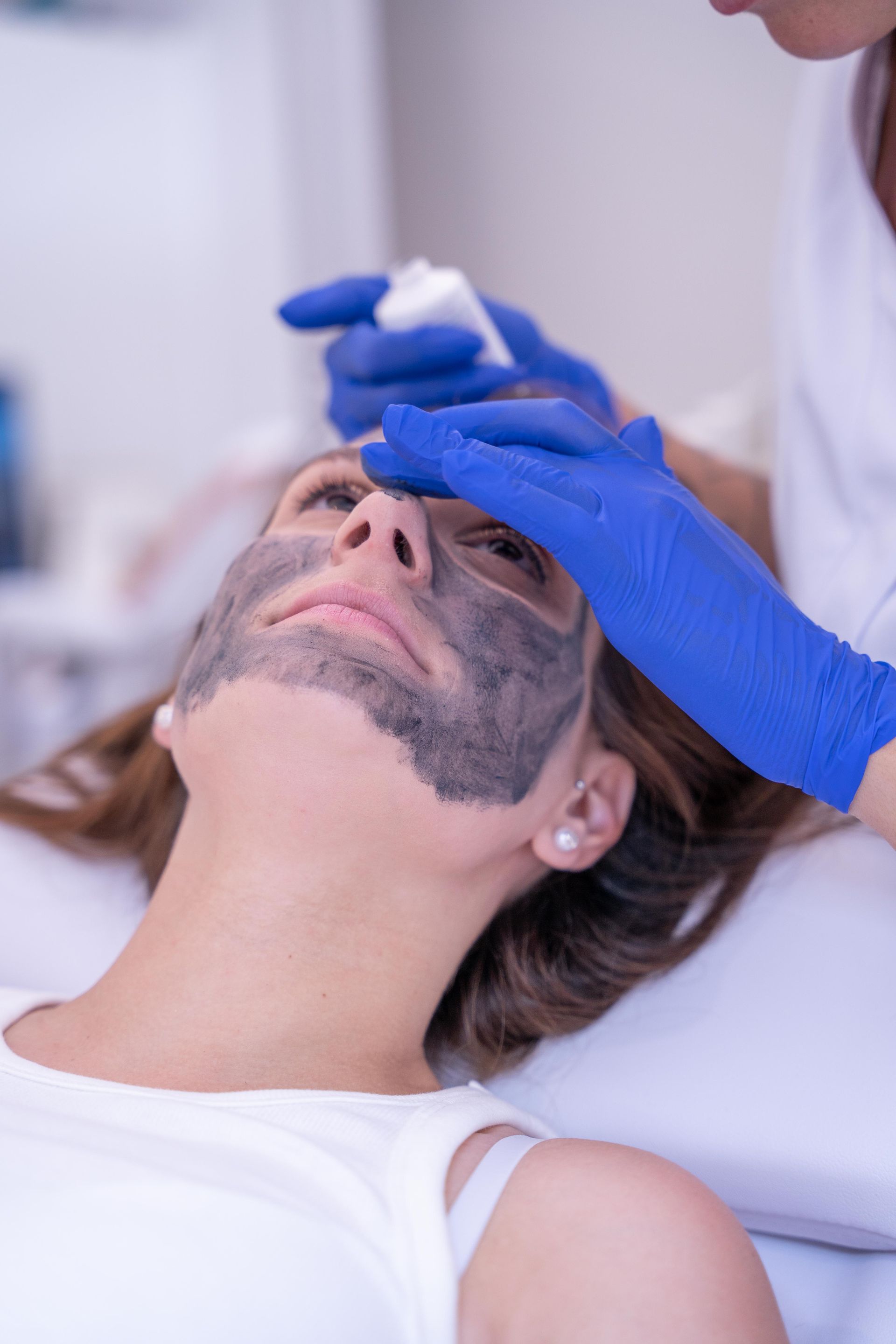Mujer recibiendo tratamiento facial, cubierta con una mascarilla oscura, en una clínica.