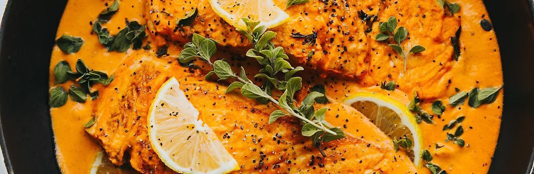Salmon fillets in a creamy orange sauce, garnished with herbs and lemon slices.