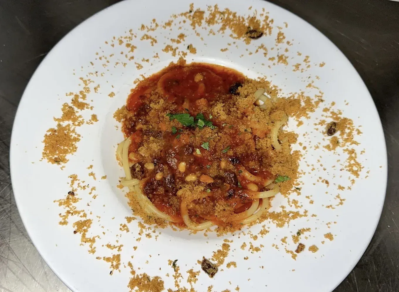 Spaghetti with red sauce, breadcrumbs, and pine nuts, served on a white plate.
