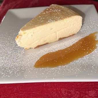 Slice of cheesecake with caramel sauce on a white plate, dusted with powdered sugar.