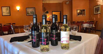 Bottles of Velar wine on a table set for dining, restaurant interior with orange walls and paintings.