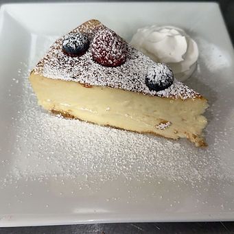 Slice of cheesecake with berries and whipped cream, dusted with powdered sugar. Served on a white plate.