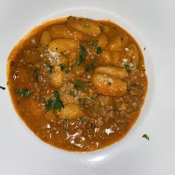 Gnocchi in orange sauce, topped with grated cheese and parsley, served in a white bowl.