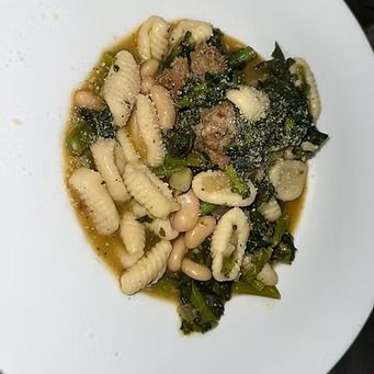 Pasta dish with sausage, white beans, and greens, sprinkled with cheese.