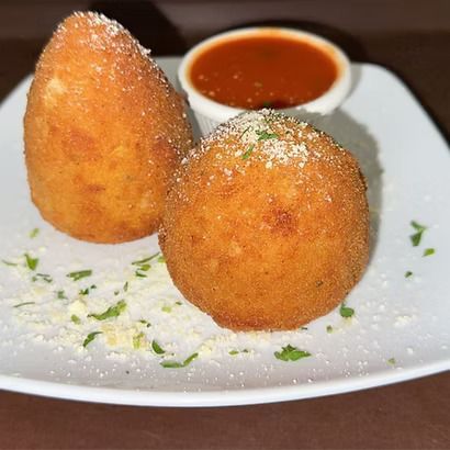 Two golden-brown arancini on a plate with red sauce. Garnished with cheese and herbs.