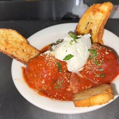 Meatballs in red sauce topped with ricotta, with garlic bread in a white bowl.