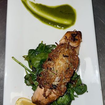 Salmon topped with crispy potato, spinach, and green sauce on a white plate with lemon.