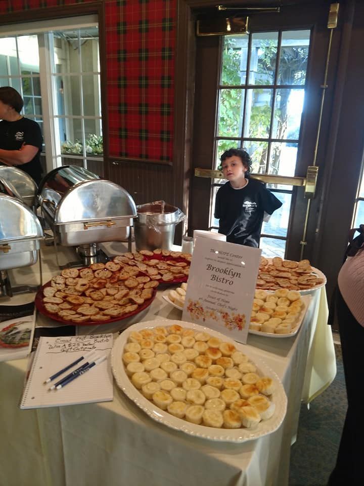 Buffet table with various appetizers, and a server behind. Plaid wall and large windows in background.