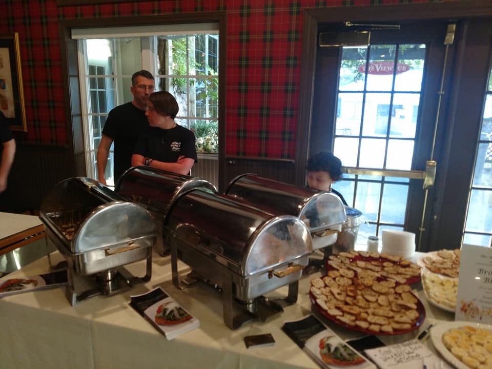 Food service table with chafing dishes, pie, and people in a room with plaid walls.